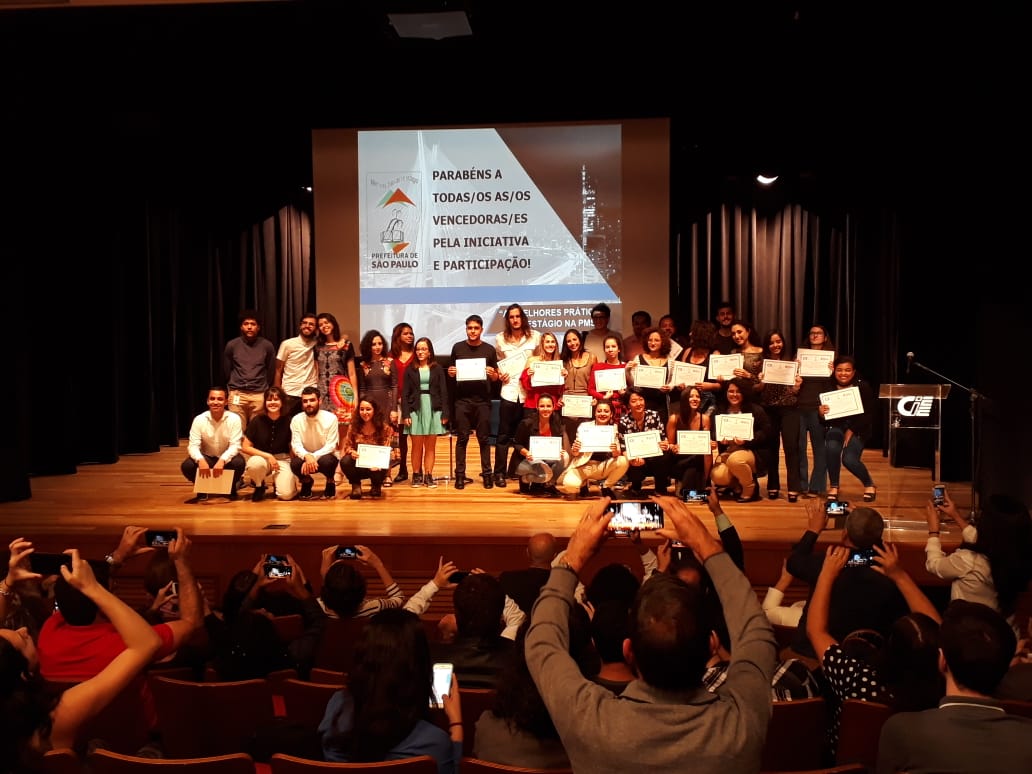 Estagiários premiados no palco, mais de 40 pessoas na foto. 